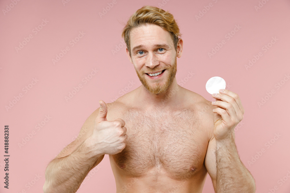 Smiling bearded naked young man 20s years old perfect skin showing thumb up hold cotton pad isolated on pastel pink color background studio portrait. Skin care healthcare cosmetic procedures concept. Smiling bearded naked young man 20s years old perfect skin showing thumb up hold cotton pad isolated on pastel pink color background studio portrait. Skin care healthcare cosmetic procedures concept.