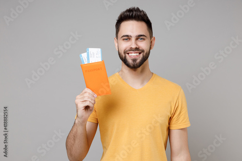 Traveler young tourist smiling man 20s in casual yellow t-shirt hold passport tickets look camera isolated on grey background. Passenger travel abroad on weekends getaway. Air flight journey concept.
