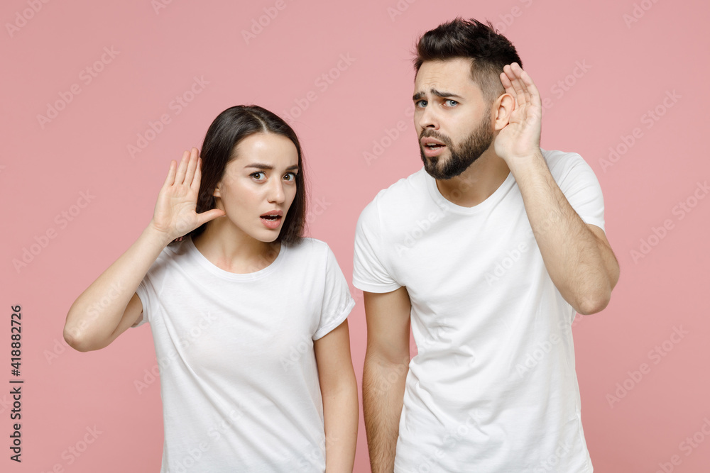 Young cheerful couple two friends bearded man brunette woman in white basic blank print design t-shirts posing looking camera standing smiling isolated on pastel pink color background studio portrait.