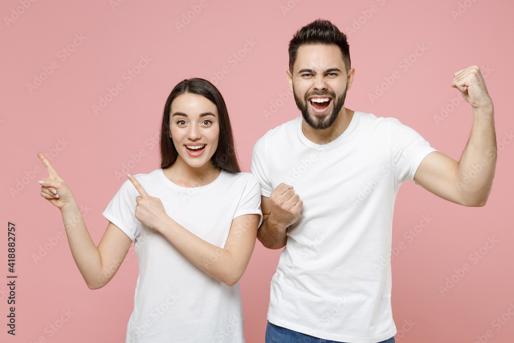 Young cheerful couple two friends man woman in white basic blank print design t-shirt pointing aside on workspace commercial area copy space mock up isolated on pastel pink background studio portrait Young cheerful couple two friends man woman in white basic blank print design t-shirt pointing aside on workspace commercial area copy space mock up isolated on pastel pink background studio portrait