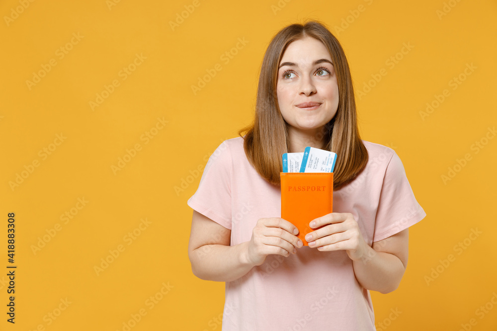 Traveler dreamful wistful tourist woman in pastel pink t-shirt hold passport, tickets look aside isolated on yellow background. Passenger travel abroad, weekends getaway. Air flight journey concept. Traveler dreamful wistful tourist woman in pastel pink t-shirt hold passport, tickets look aside isolated on yellow background. Passenger travel abroad, weekends getaway. Air flight journey concept.