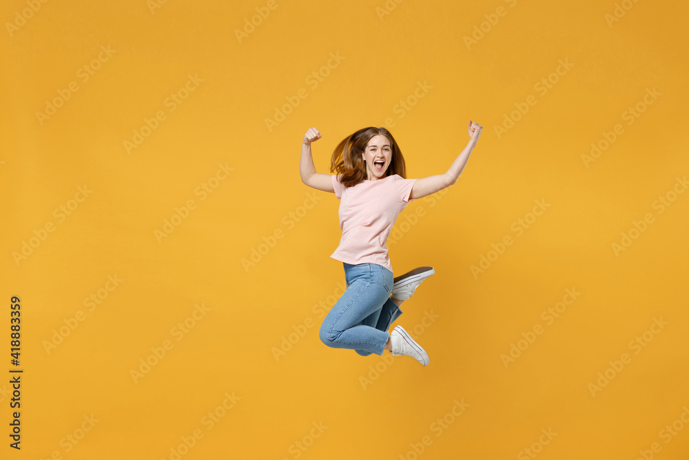 Full length of young overjoyed expressive happy woman 20s wearing casual basic pastel pink t-shirt jumping high do winner gesture clench fist celebrating isolated on yellow background studio portrait.