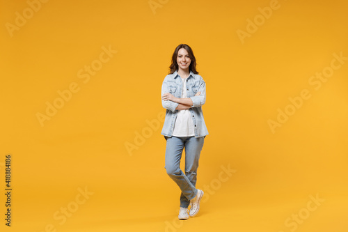 Full length of young caucasian smiling happy confident european cute woman 20s wearing stylish casual denim shirt white t-shirt hold hands crossed folded isolated on yellow background studio portrait