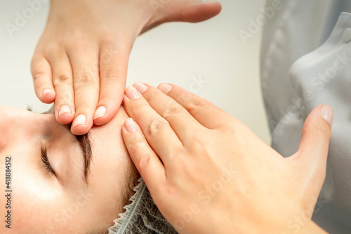 Young caucasian woman receiving facial massage by beautician s hands in spa medical salon