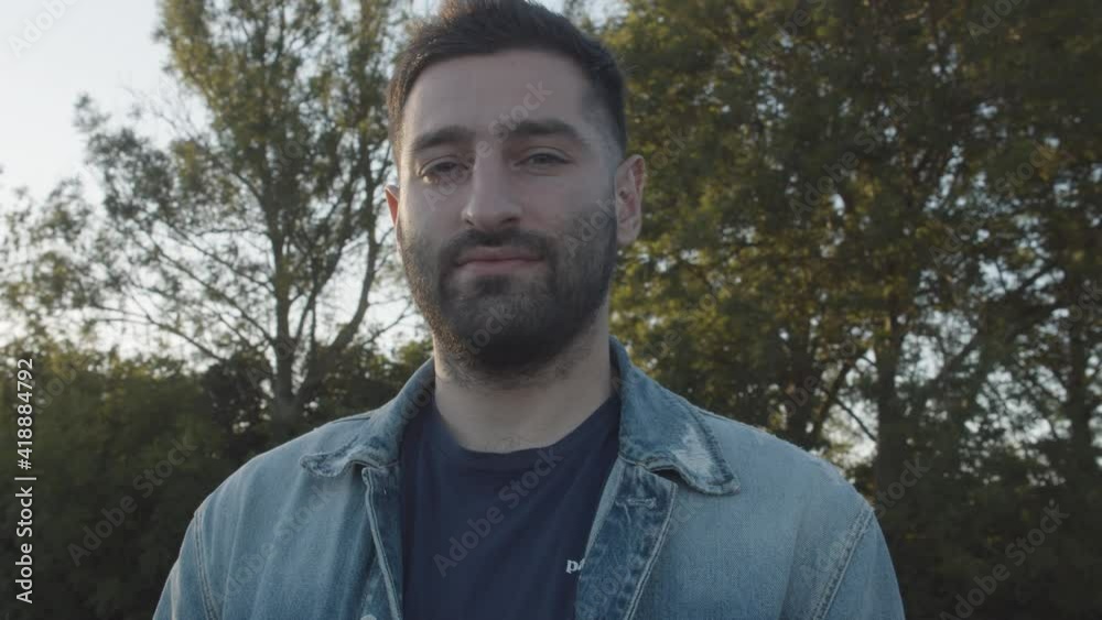Profile dolly shot of a man looking at camera, standing outside in the bright summer countryside.