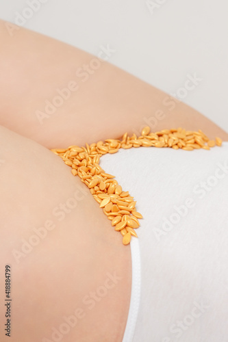 Depilation of the bikini area. Bikini zone of a young woman with wax hard beans lying down on a white background