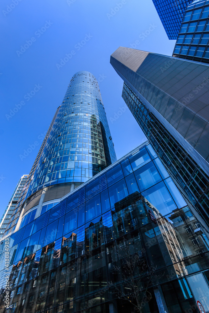 Skyscrapers and commercial buildings in the financial district of Frankfurt. Looking up along the window facade in the city center. Blue sky in sunny day. Reflections in the glass facade
