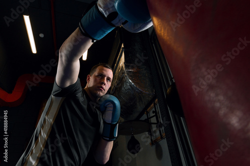 Photo From below a young male athlete in boxing gloves who beats a boxing pear in a gym. High quality photo