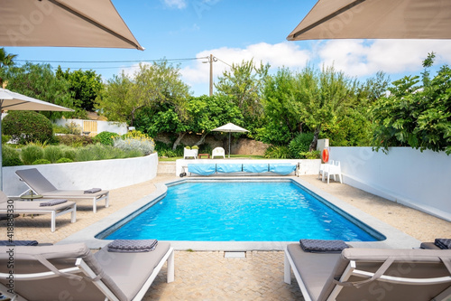 Loungers placed on the left and in the front of a pool with clean looking water on a sunny day.