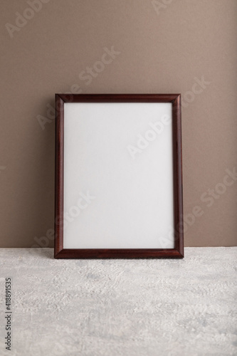 Brown wooden frame mockup on beige paper background. Blank, vertical orientation, still life.