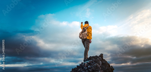 Hiker with backpack raising arms up on the top of the mountain - Successful man celebrating victory  photo