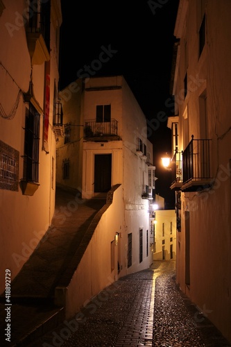 The deserted narrow cobbled alleys of Arcos de la Frontera, Spain, by night, the white facades warmly lit by vintage street lights