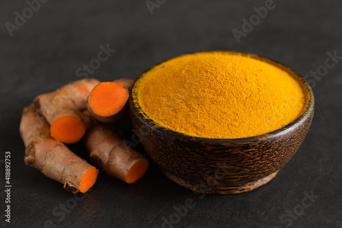 Turmeric powder in a black wooden bowl and fresh turmeric (curcumin) on black background,spices.