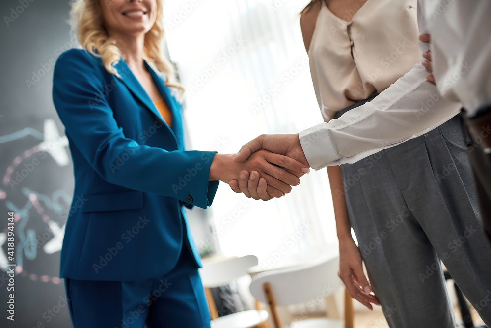 Close up of female broker and male client shaking hands while making a deal after signing papers, purchasing flat or house