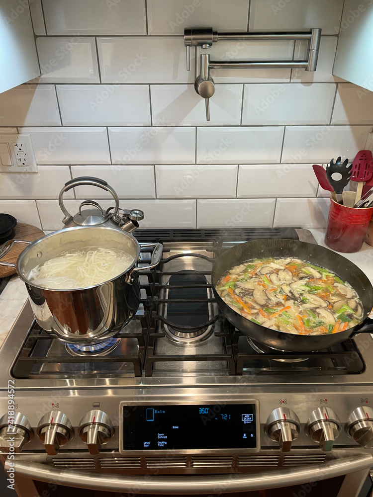 New York. 2021. Chinese meal being cooked using a wok. Noodles and chickem, mushrooms, scallions, carrot cooking on a modern gas oven. New York. 2021. Chinese meal being cooked using a wok. Noodles and chickem, mushrooms, scallions, carrot cooking on a modern gas oven.