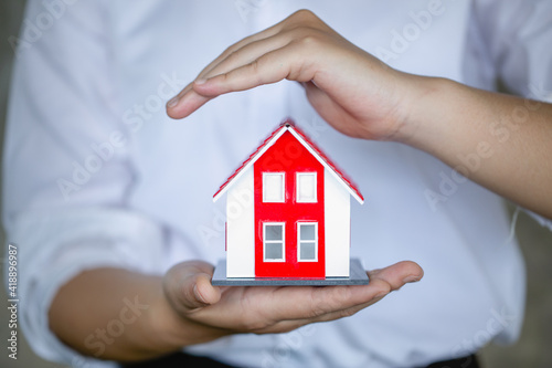 A red roof house that businessmen are using their hands to protect The concept of the use of gestures in real estate investors, leasing insurance, purchase and sales contracts and maintenance.