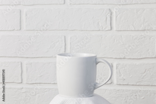 Household utensils, a white cup stands on a napkin against the background of a kitchen stone brick wall of a milky shade, the concept of clean dishes