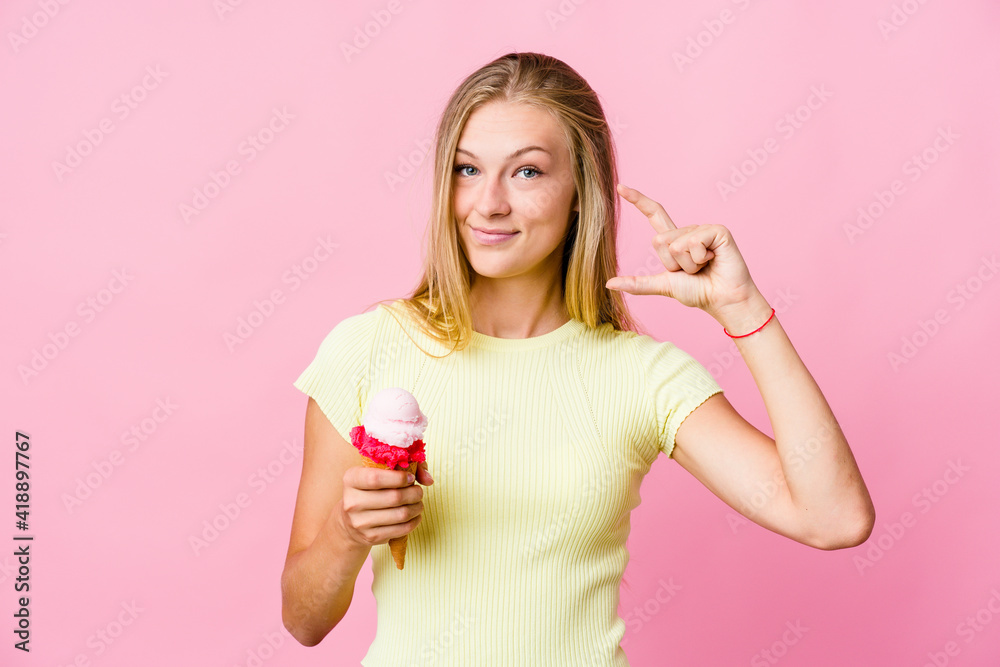 Young russian woman eating an ice cream isolated holding something little with forefingers, smiling and confident. Young russian woman eating an ice cream isolated holding something little with forefingers, smiling and confident.