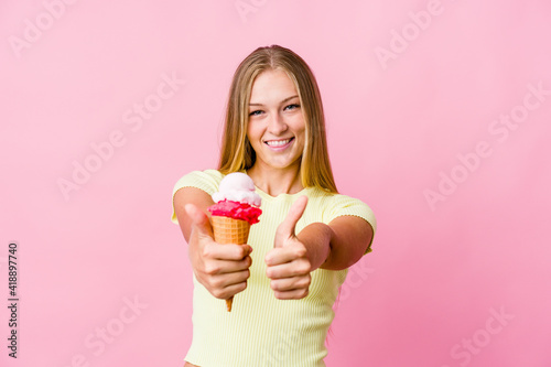Young russian woman eating an ice cream isolated with thumbs ups, cheers about something, support and respect concept.