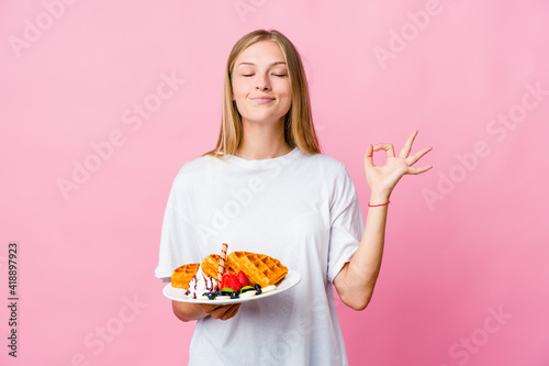 Young russian woman eating a waffle isolated relaxes after hard working day, she is performing yoga.