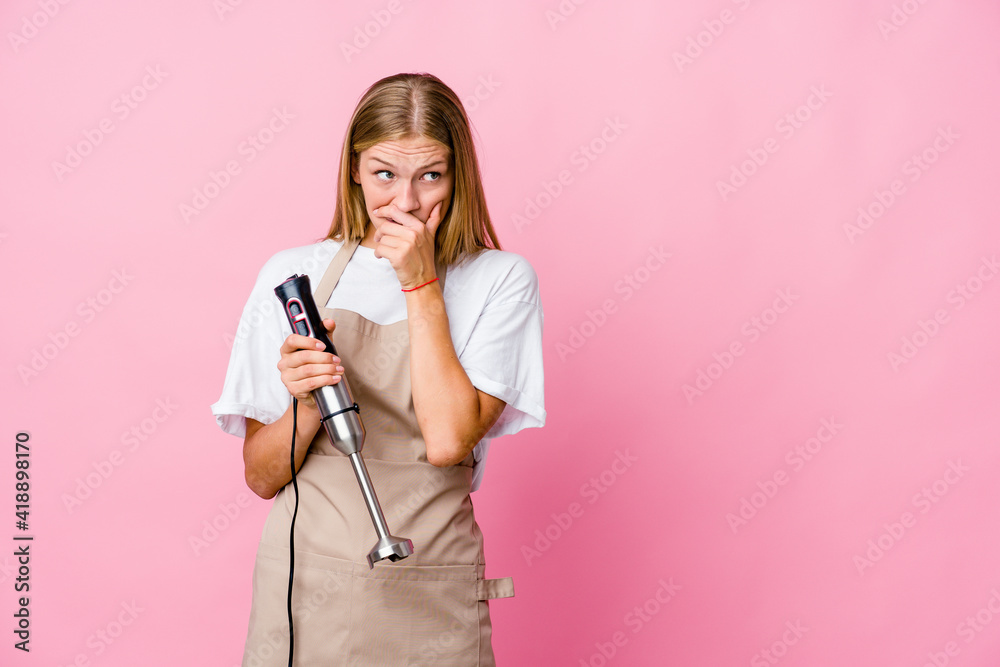 Young russian cook woman holding an electric mixer isolated thoughtful looking to a copy space covering mouth with hand. Young russian cook woman holding an electric mixer isolated thoughtful looking to a copy space covering mouth with hand.