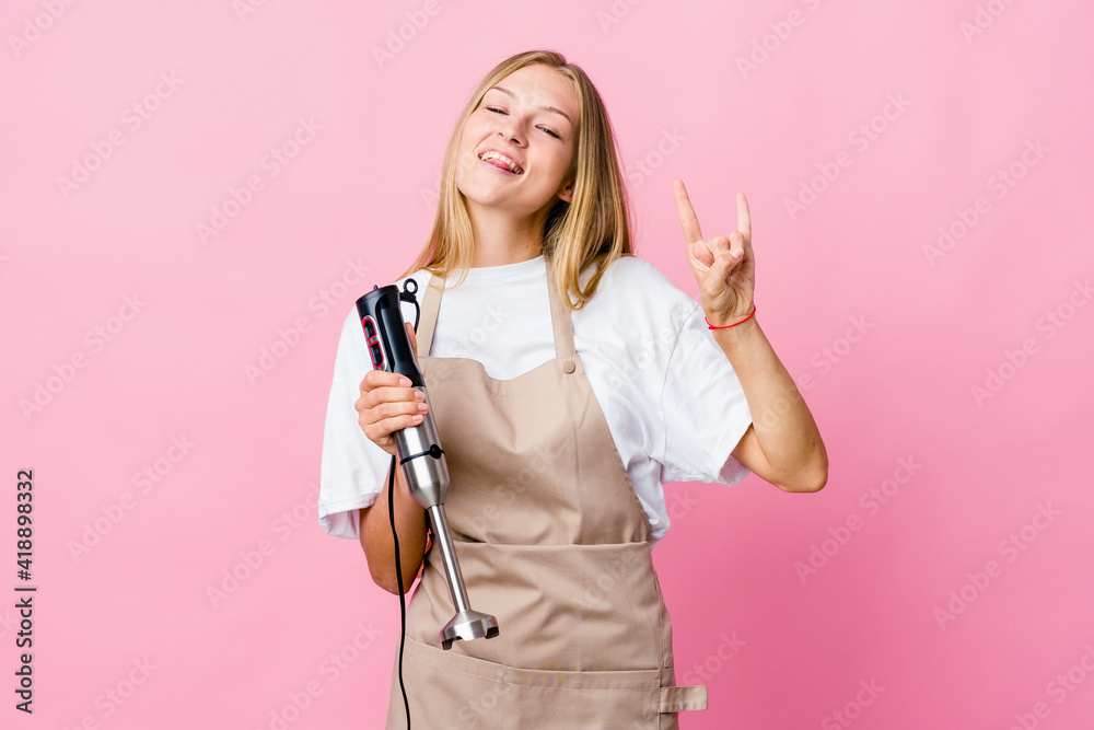 Young russian cook woman holding an electric mixer isolated showing a horns gesture as a revolution concept.