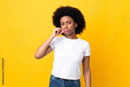 Young African American woman isolated on yellow background showing a sign of silence gesture