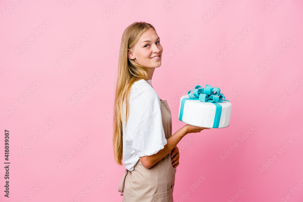 Young russian baker woman holding a delicious cake looks aside smiling, cheerful and pleasant. Young russian baker woman holding a delicious cake looks aside smiling, cheerful and pleasant.