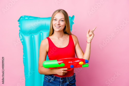 Young russian woman playing with a water gun with an air mattress smiling cheerfully pointing with forefinger away.