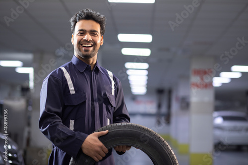 Portrait of smiling mechanic holding a tyre in auto repair shop 