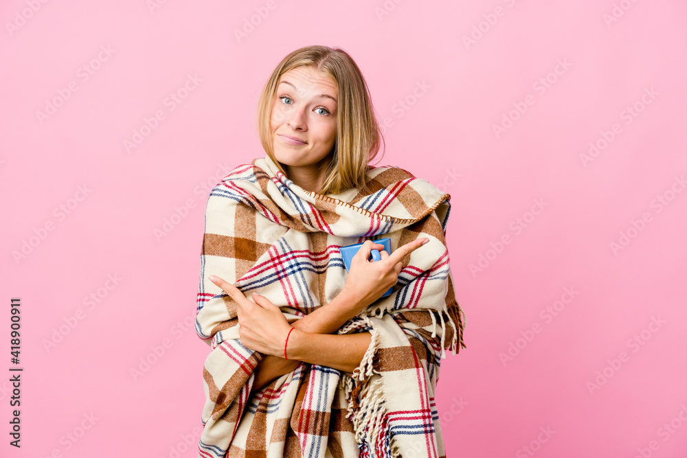 Young russian woman wrapped in a blanket drinking coffee points sideways, is trying to choose between two options. Young russian woman wrapped in a blanket drinking coffee points sideways, is trying to choose between two options.