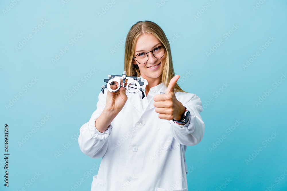 Young russian optometrist woman on blue with thumbs ups, cheers about something, support and respect concept. Young russian optometrist woman on blue with thumbs ups, cheers about something, support and respect concept.