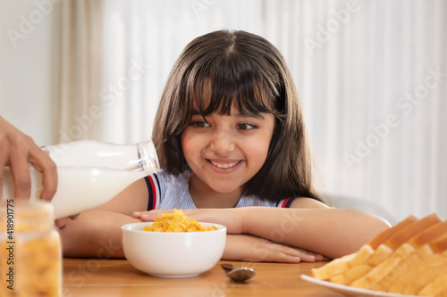 A SMALL GIRL HAPPILY SITTING AND LOOKING AT MILK BEING SERVED	