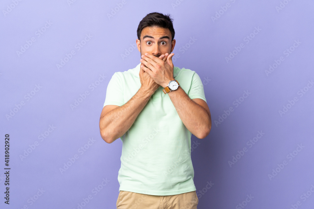 Young handsome man isolated on purple background covering mouth with hands Young handsome man isolated on purple background covering mouth with hands