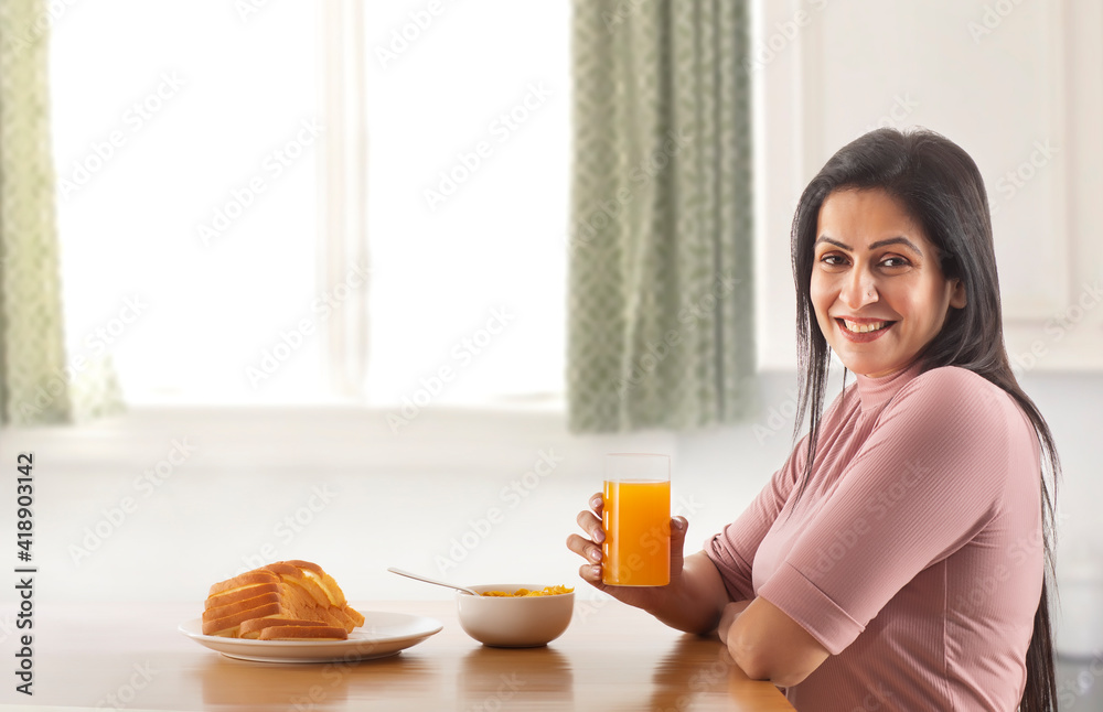 A HAPPY WOMAN SITTING AND LOOKING AT CAMERA WHILE HOLDING A GLASS OF FRESH JUICE A HAPPY WOMAN SITTING AND LOOKING AT CAMERA WHILE HOLDING A GLASS OF FRESH JUICE