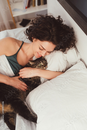 Happy young woman spending time with her cat in bed at home