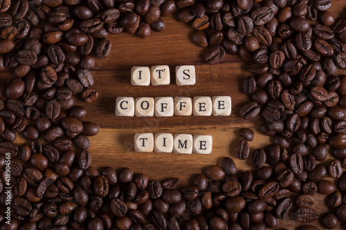Beans Coffee all around on a wooden table. it s coffee time with a wooden cube letters.