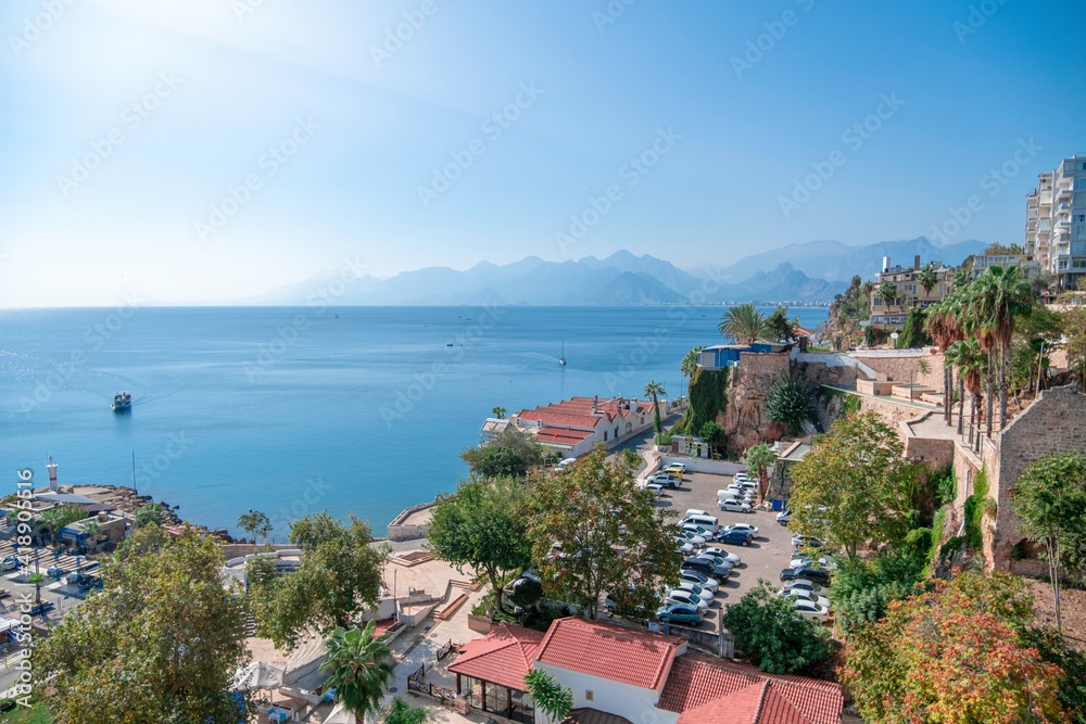 View of the resort town, houses with red roofs, the sea, beautiful mountains in the haze on the horizon and yachts floating on the water on a sunny day
