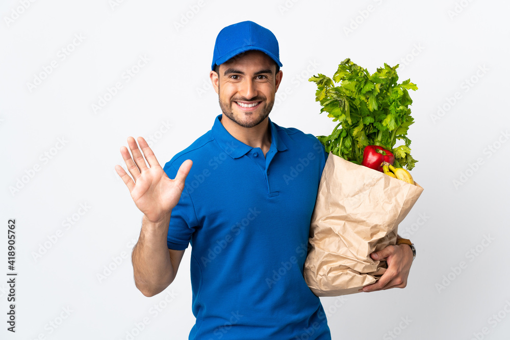 Delivery man with vegetables isolated on white background saluting with hand with happy expression Delivery man with vegetables isolated on white background saluting with hand with happy expression