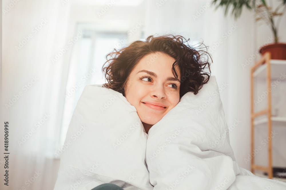 Woman keeping smile on her face while looking away wrapped at the white blanket Woman keeping smile on her face while looking away wrapped at the white blanket