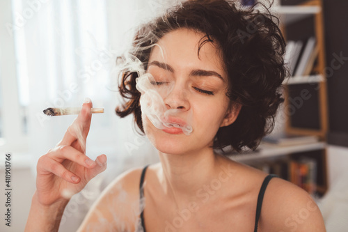 Woman spending time in bed at home while smoking marijuana