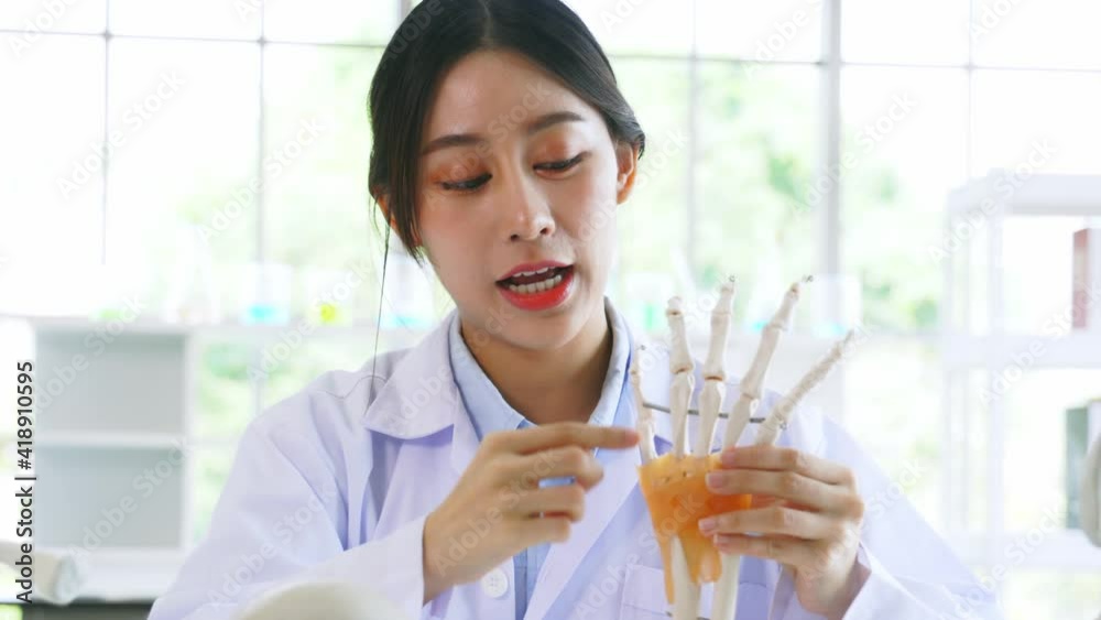 Portrait of young Asian woman doctor wearing lab coat preparing a bone model to describe symptoms to patient while working in hospital Portrait of young Asian woman doctor wearing lab coat preparing a bone model to describe symptoms to patient while working in hospital