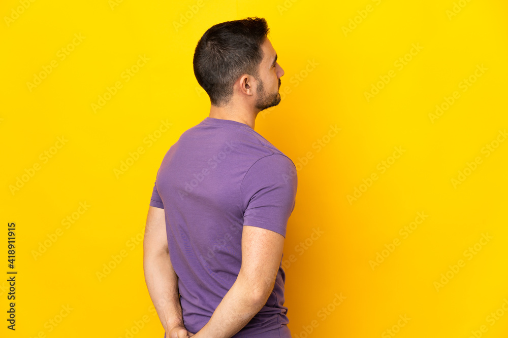 Young caucasian handsome man isolated on yellow background in back position and looking back Young caucasian handsome man isolated on yellow background in back position and looking back
