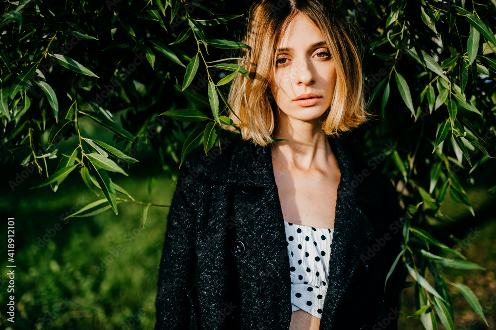 Portrait of elegant stylish blonde short hair girl posing in the park over green branches Portrait of elegant stylish blonde short hair girl posing in the park over green branches
