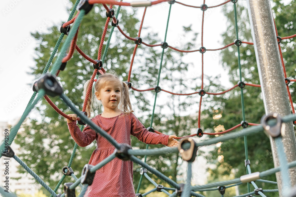 Happy little girl playing on the playground. Kid having fun with the climbing net outdoors
