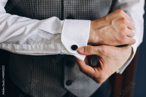 Wedding. The groom. Business. A young man in a white shirt and vest straightens cufflinks on his sleeves photo