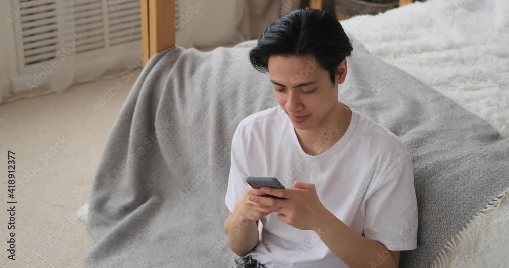Man text messaging on mobile phone in bedroom at home