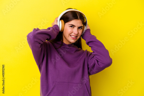 Young caucasian woman listening to music with headphones isolated on pink background covering ears with hands. © Asier