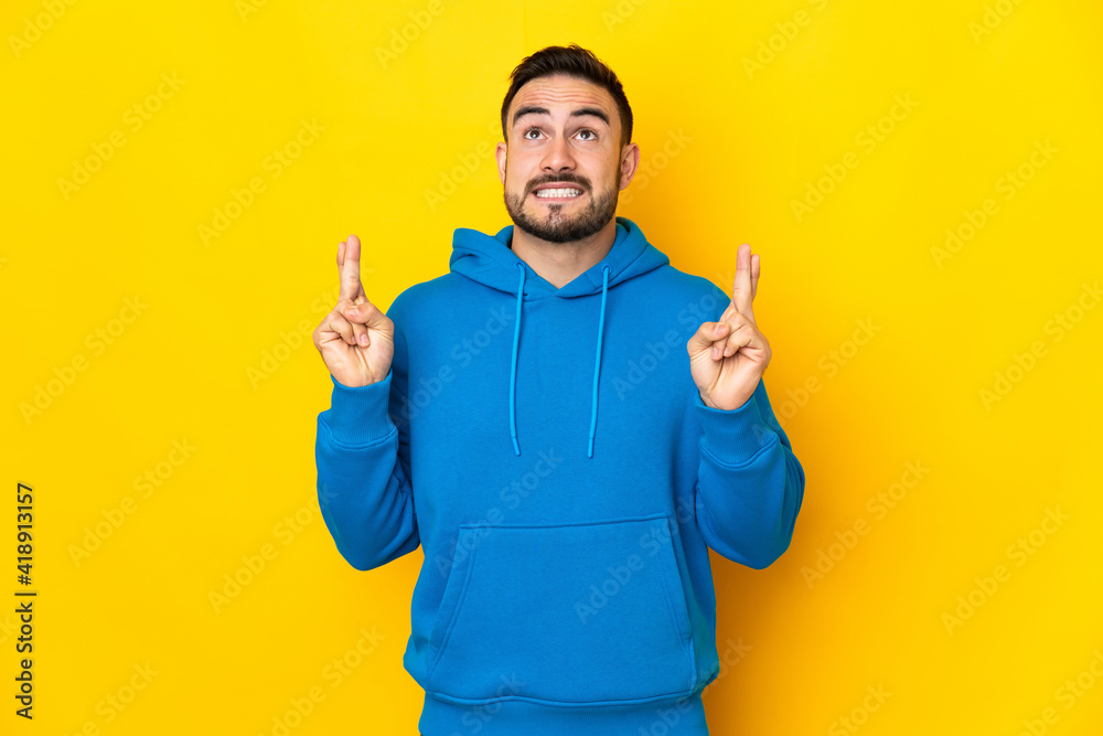 Young caucasian handsome man isolated on yellow background with fingers crossing and wishing the best Young caucasian handsome man isolated on yellow background with fingers crossing and wishing the best