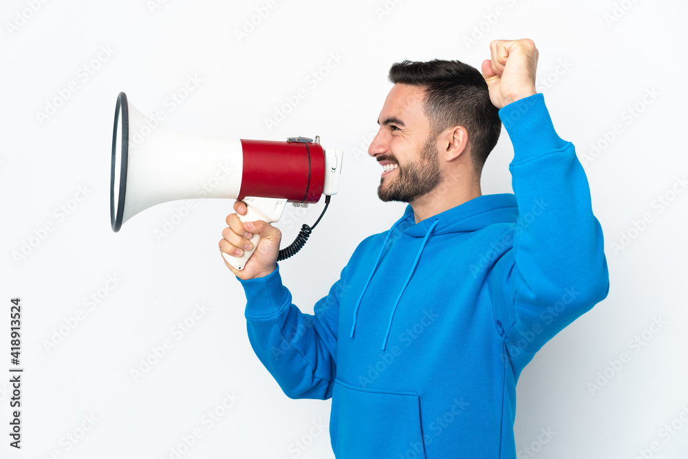 Young caucasian handsome man isolated on white background shouting through a megaphone to announce something in lateral position Young caucasian handsome man isolated on white background shouting through a megaphone to announce something in lateral position